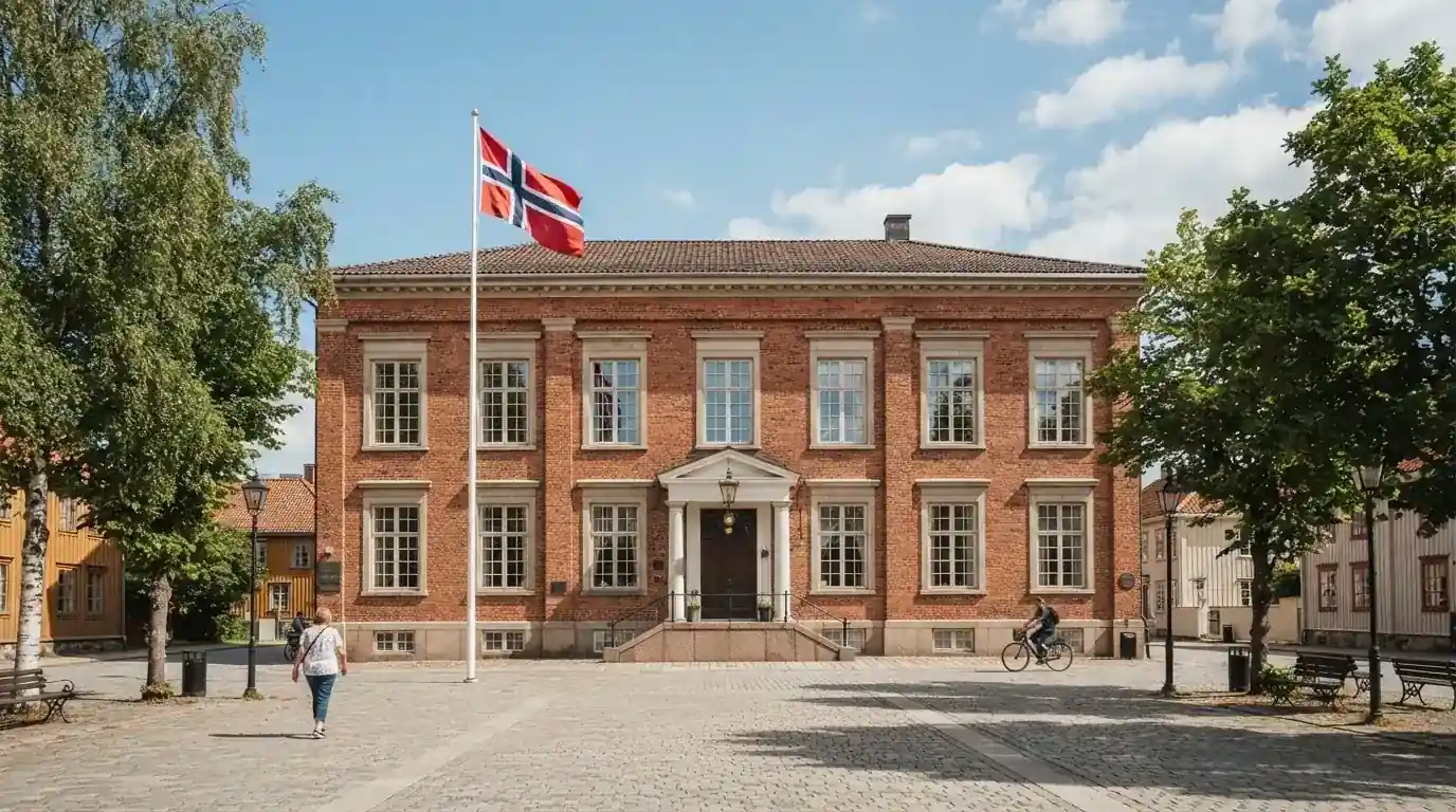 Offentlig kontorbygning i rødt murstein i en norsk by, med et flagg ved inngangen og blå himmel