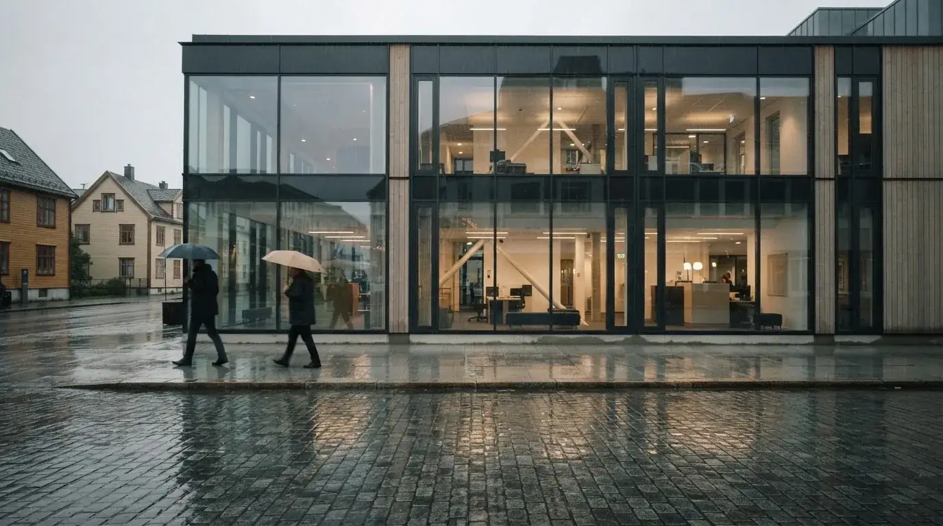 Bankfilial med store vinduer i en norsk by i regnvær, noen med paraplyer utenfor